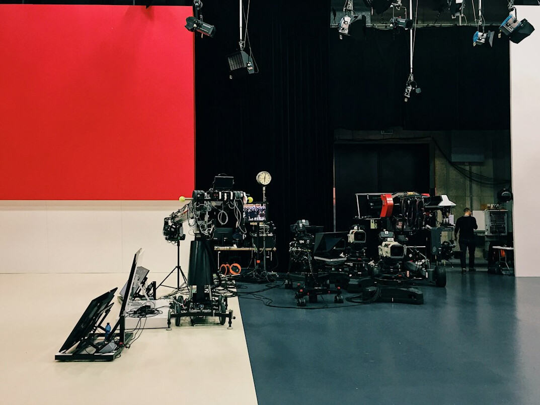 Wide view of a television studio set with cameras and bright lighting rigs